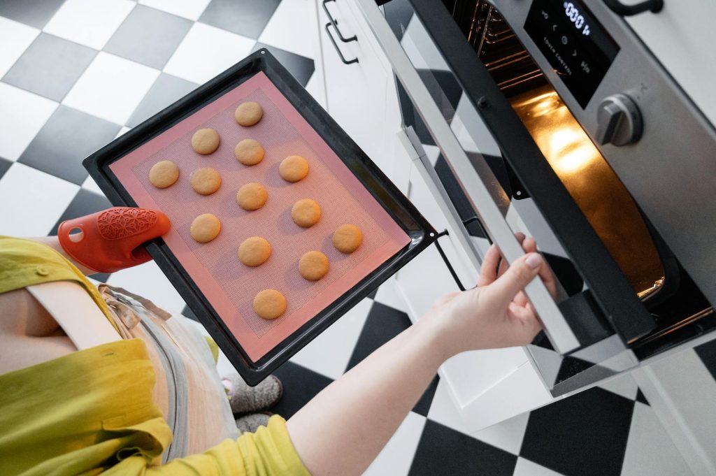 crop woman putting cookies in oven in kitchen